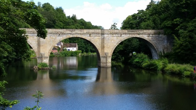 Stone, 2-arched bridge across the Wear River, with old mill in the background. Similar to bridge built in the novel - An Uncertain Age