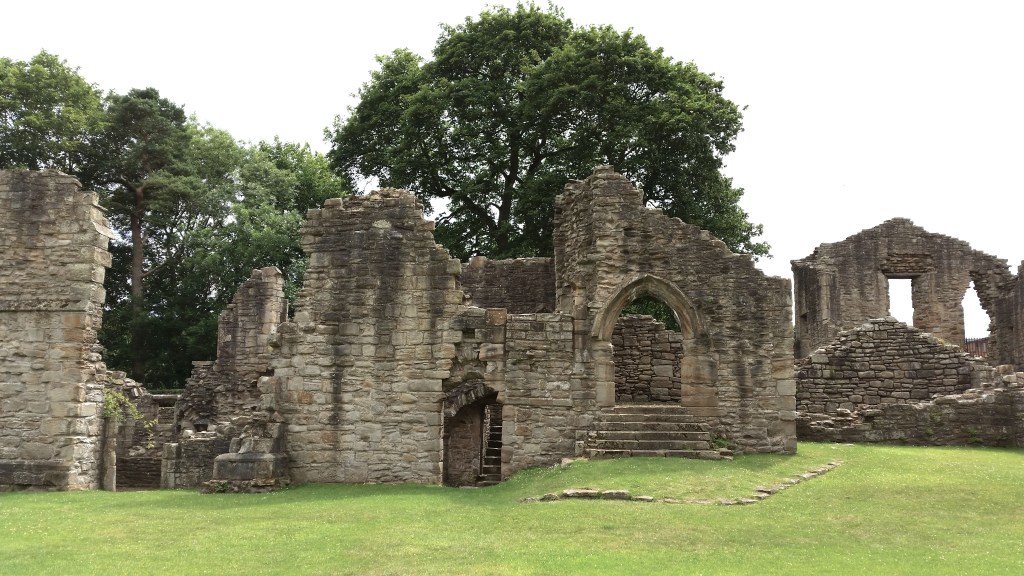 Ruined walls of Finchdale Priory in grey stone, trees in the background.