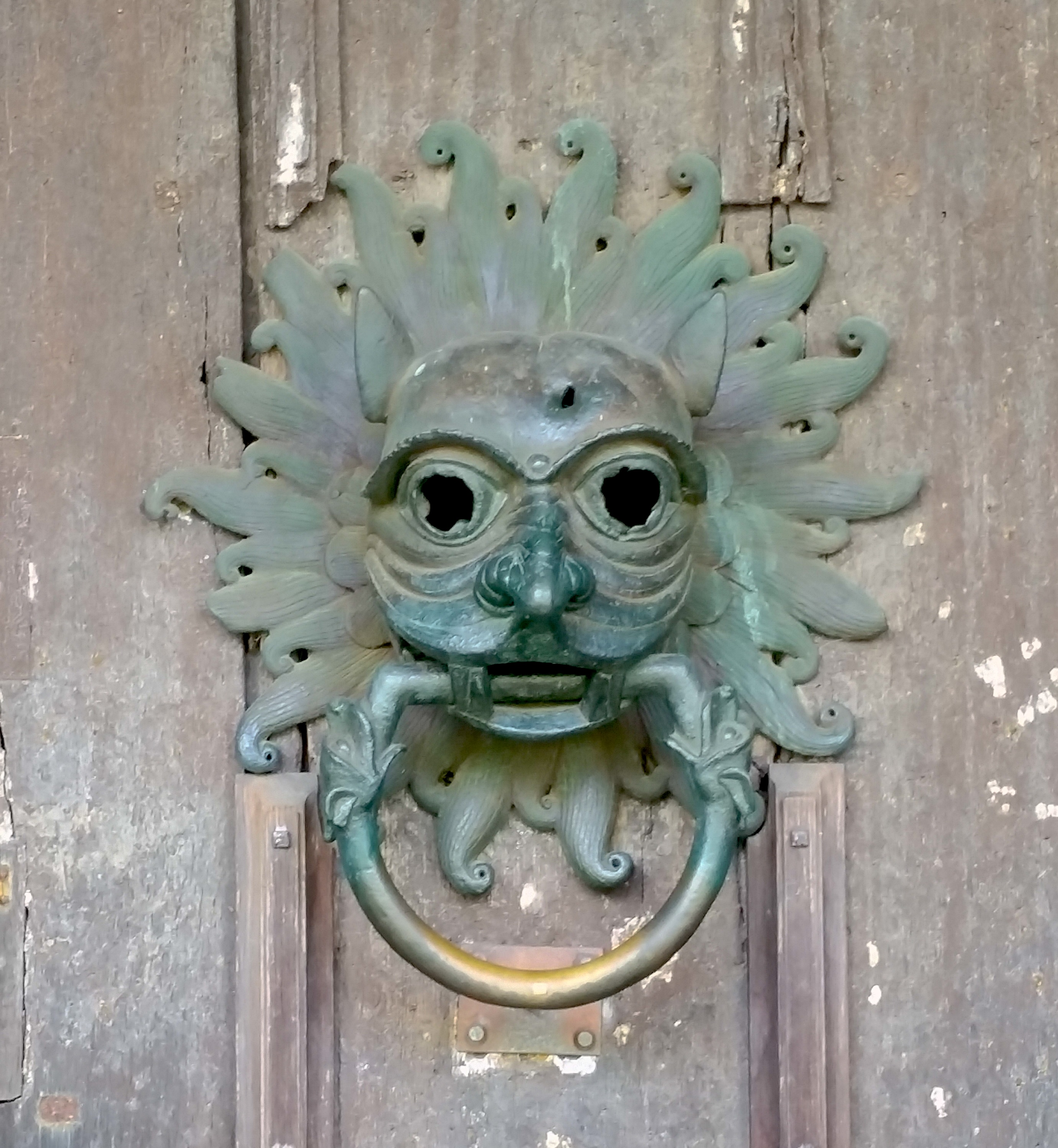 Sanctuary door knocker, Durham Cathedral. Stylized lion's head, brass, verdigris, on wooden paneled door.